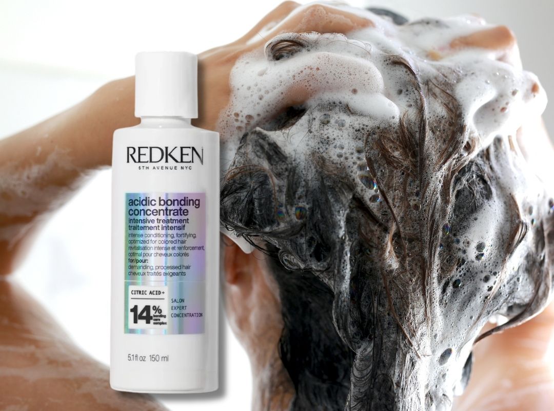 A bottle of Redken Acidic Bonding Concentrate is shown in front of a person washing their hair with soapy lather, demonstrating the product's use.