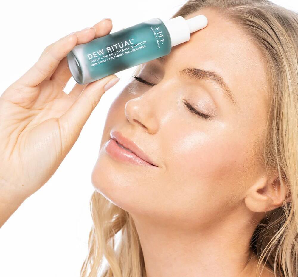 Woman applying a skincare serum to her face with a white background
